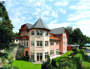 Ein mehrstöckiges Gebäude mit einem zentralen Turm, großen Fenstern und einem gepflegten Garten.
