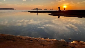 En strandscen med stilla vatten som speglar himlen, en person som står på sanden och en annan person på avstånd.
