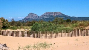 En sandstrand med ett trästaket och gles vegetation i förgrunden, som leder fram till ett bergskedja i bakgrunden.