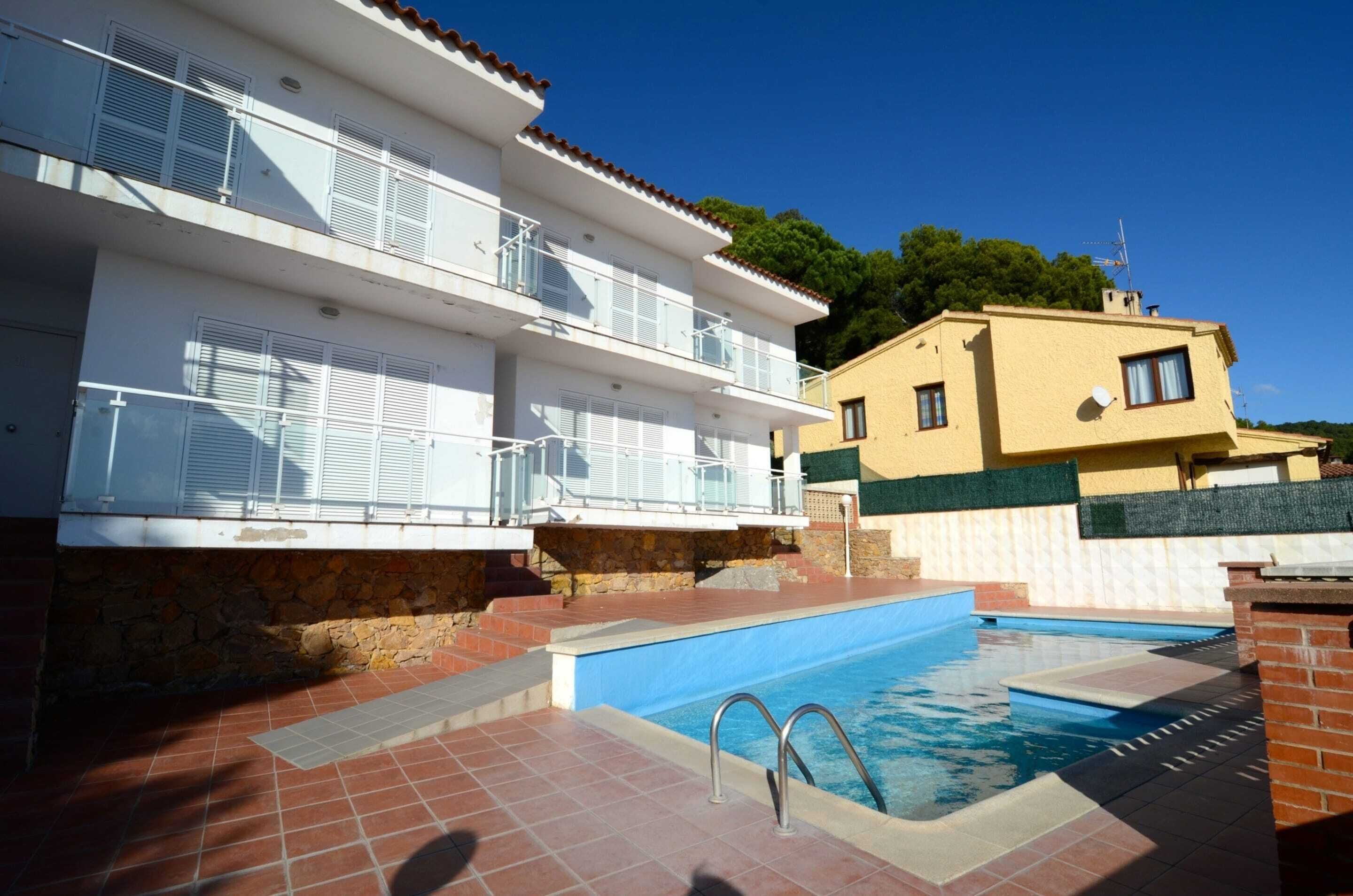 A multi-story building with balconies, a swimming pool, and a stone wall.