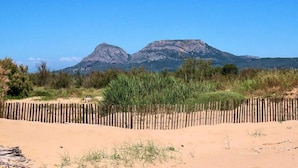 En sandstrand med ett trästaket och gles vegetation i förgrunden, som leder fram till ett bergskedja i bakgrunden.
