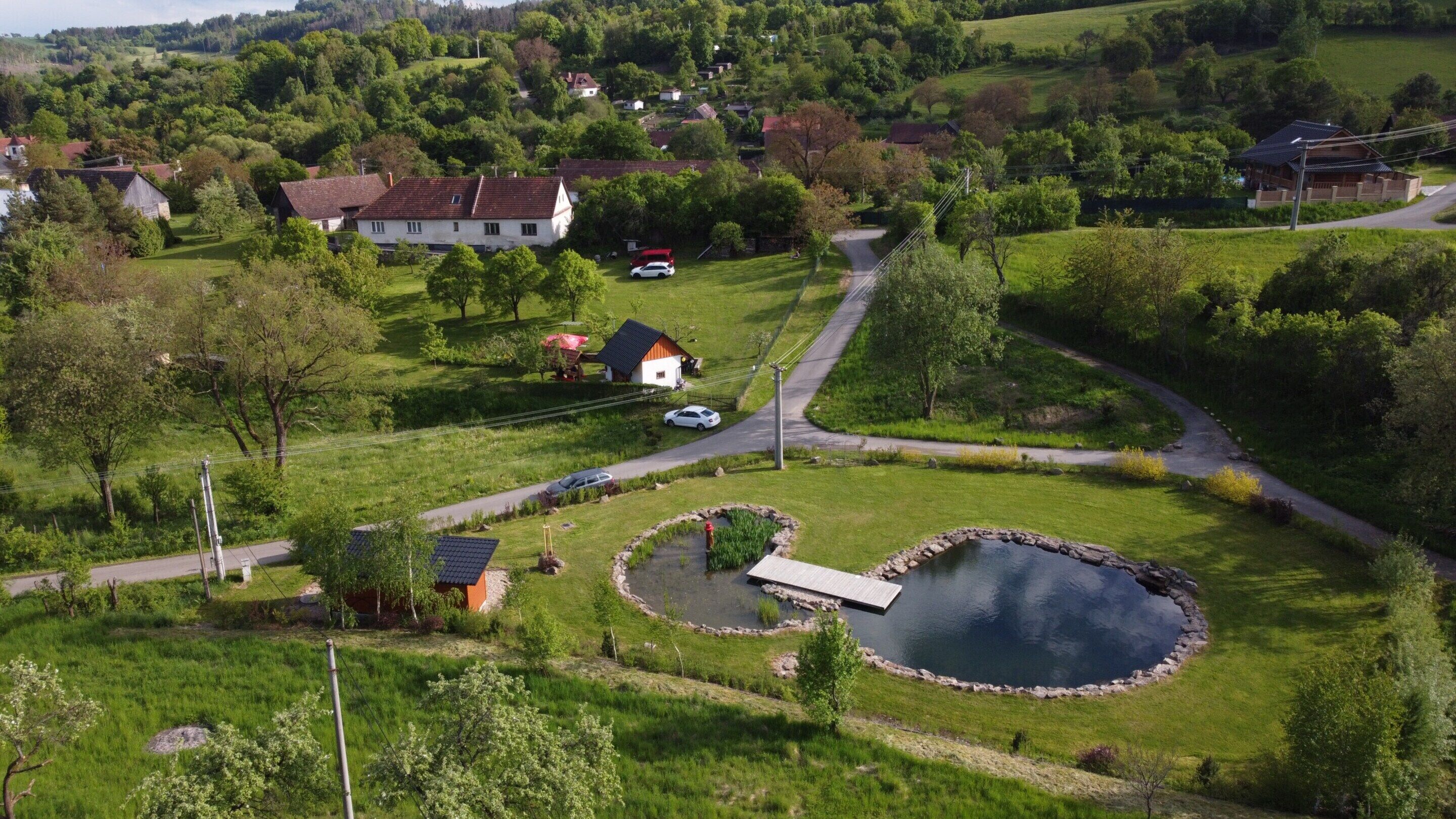 Eine Luftaufnahme einer ländlichen Gegend mit Häusern, einem Teich und einer kurvenreichen Straße.