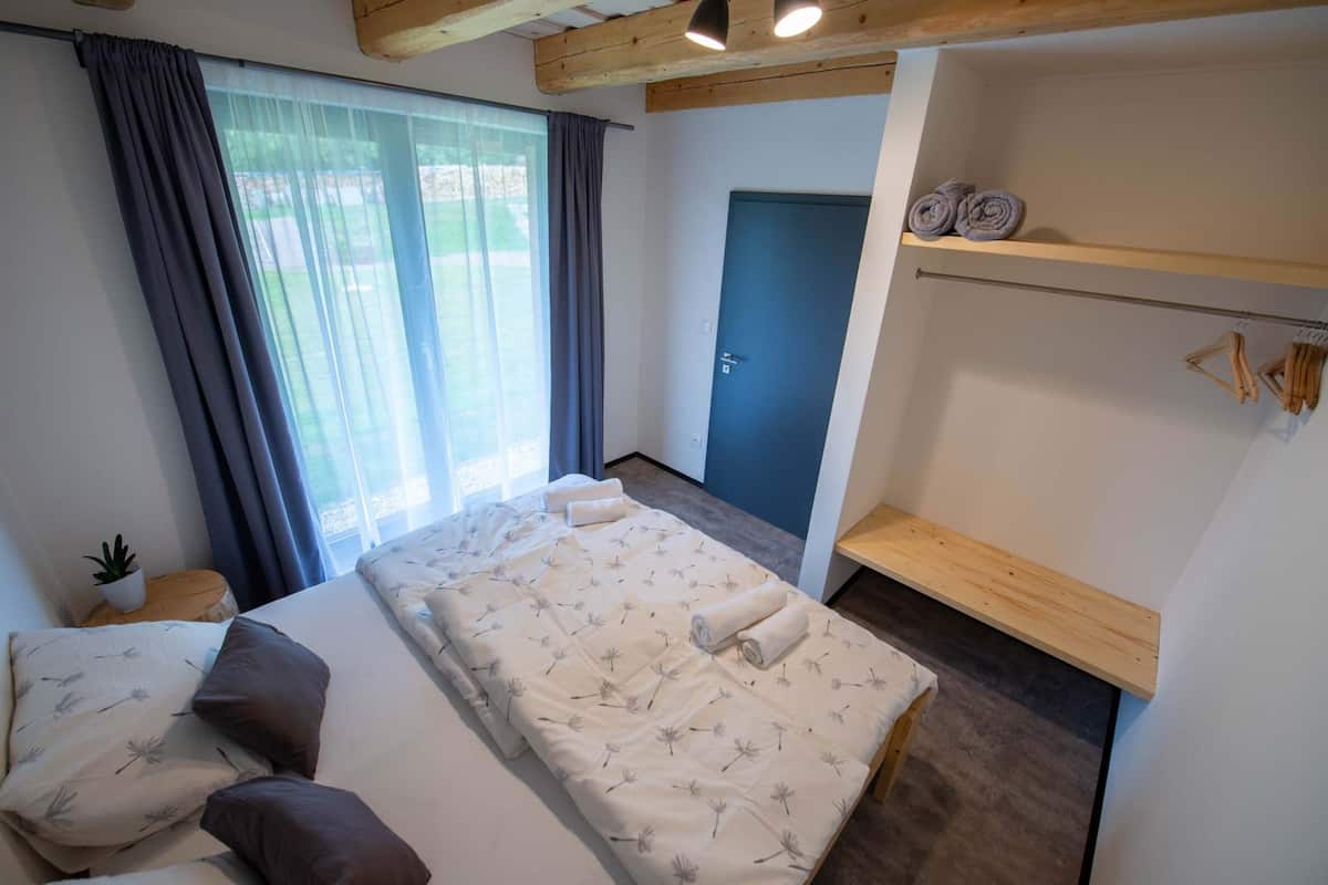 Ett sovrum med en säng, ett fönster med gardiner, en dörr och en hylla med handdukar.
