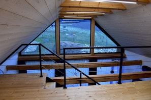 Un intérieur en bois avec un plafond incliné, un escalier et une grande fenêtre donnant sur un espace extérieur.