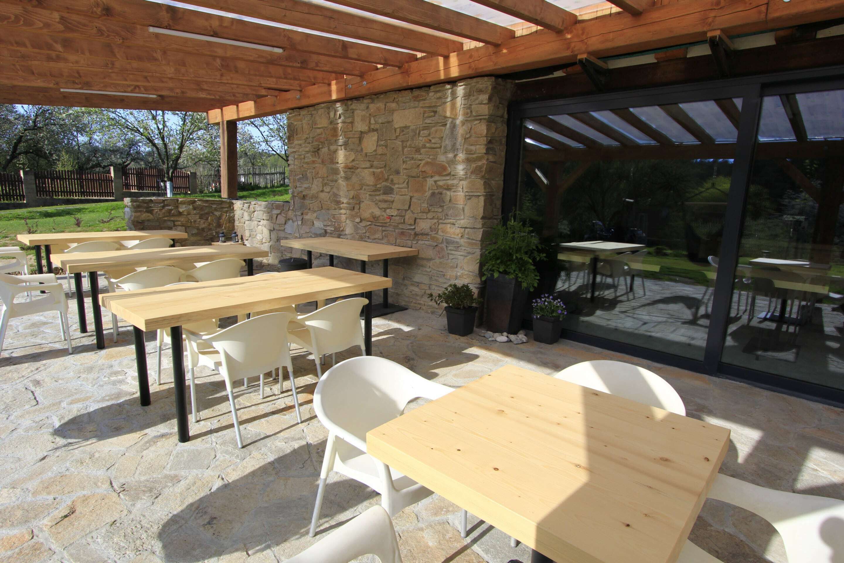 An outdoor patio with stone flooring, wooden tables, and white chairs.