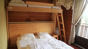 Ein Schlafraum mit Etagenbetten, einem Holz-Kopfteil, einer Leiter und einem Fenster mit Vorhängen.