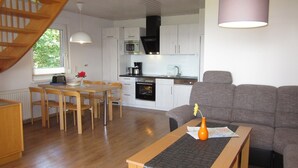 Eine moderne Küche mit weißen Schränken, ein Essbereich mit Holzsesseln und ein graues Sofa.