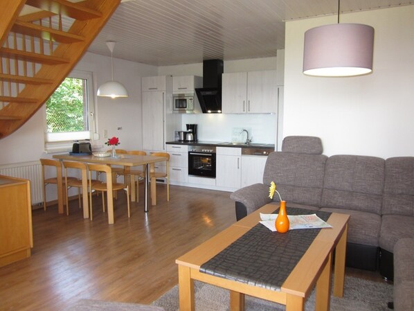 Een moderne keuken met witte kasten, een eethoek met houten stoelen en een grijze bank.