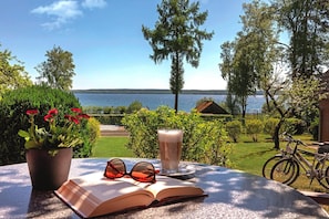 An open book, a pair of sunglasses, and a glass of beverage on a table with a view of a lake and greenery. - Seepark Heidenholz, Plau am See (Plau am See)