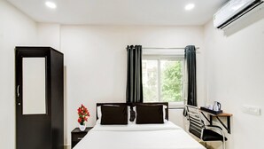 A hotel room with a bed, a desk, a chair, a window with curtains, an air conditioner, and a door. - Townhouse Near Narsingi Manikonda (Hyderabad)