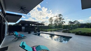 Un espace piscine extérieur moderne, doté de chaises longues, d’un ventilateur de plafond et offrant une vue dégagée sur le paysage environnant.