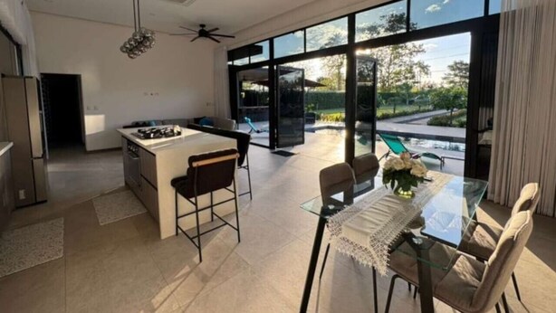 Une cuisine moderne dotée d’un îlot central, d’un coin repas avec une table en verre et de grandes fenêtres offrant une vue sur l’extérieur.