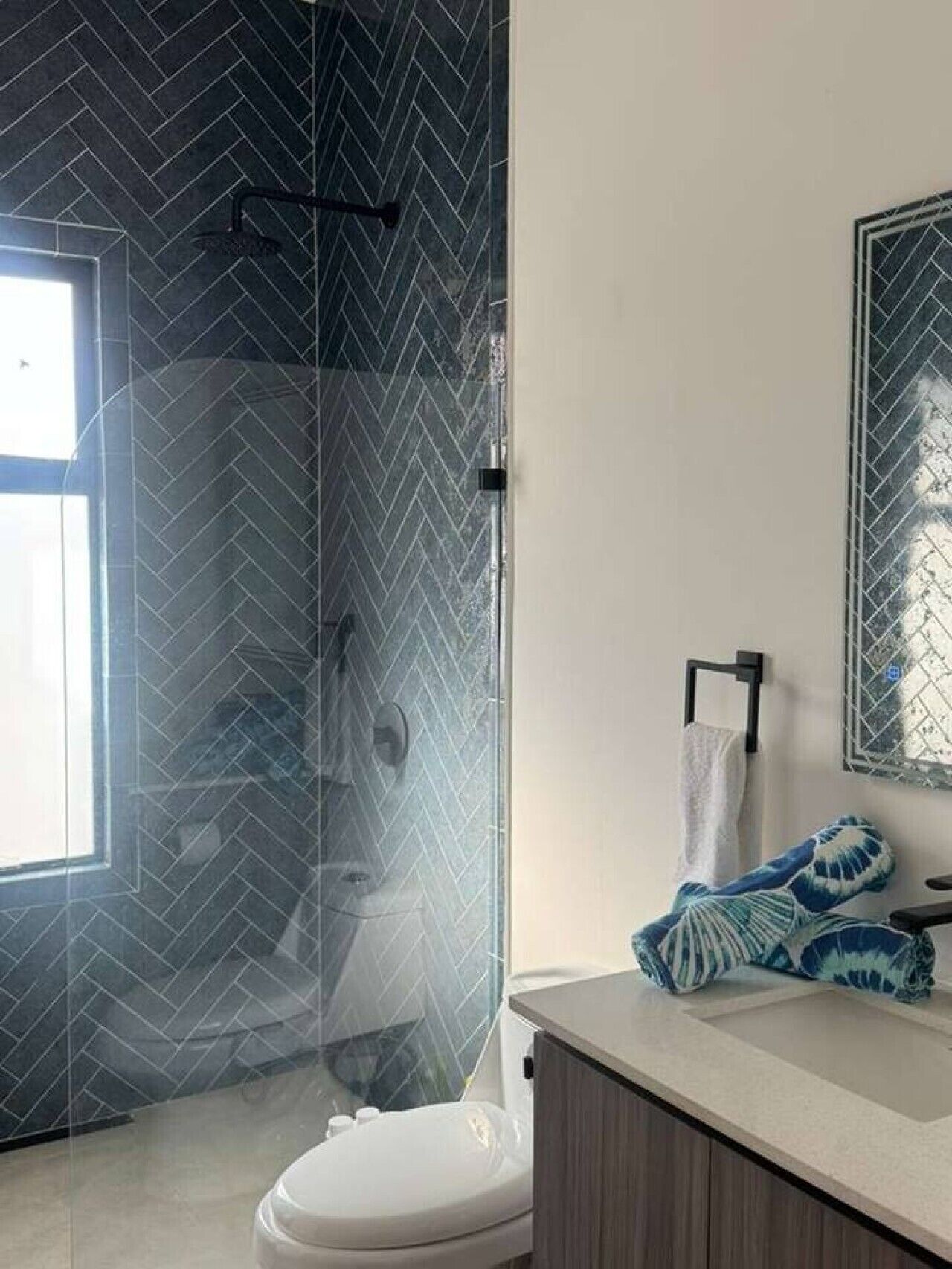 Un baño con cabina de ducha de vidrio, inodoro, lavamanos con toalla y espejo.