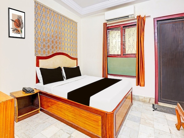 A bedroom with a bed, a bedside table with a phone, a patterned wall, a window with curtains, and a door.