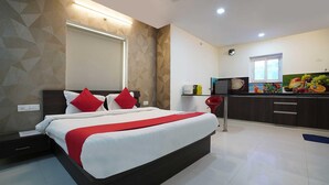 Ein modernes Hotelzimmer mit einem großen Bett, einer kleinen Küchenzeile und einem Fenster.