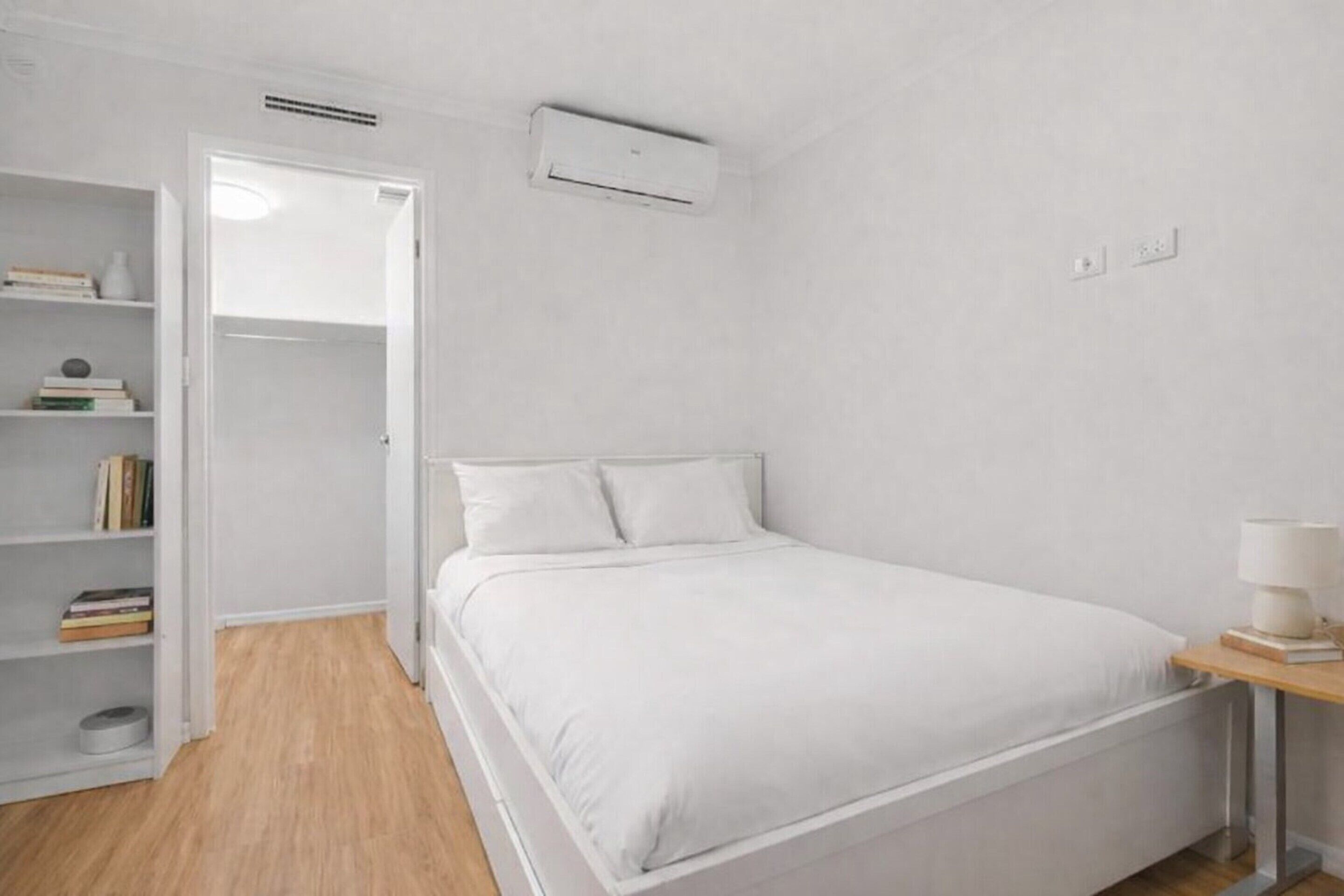 Ein Schlafzimmer mit einem Bett, einem Nachttisch mit Lampe, einem Kleiderschrank und einer Klimaanlage.