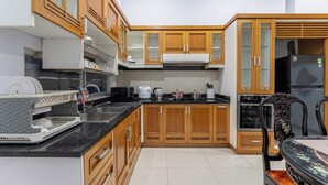 A modern kitchen with wooden cabinets, a black countertop, and a dining area with a glass table. - Group Stay in Central Saigon_ 6 Bedrooms + Private Baths (Thành phố Hồ Chí Minh)