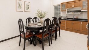 A dining area with a round table, six chairs, a vase with flowers, and framed botanical prints on the wall. - Group Stay in Central Saigon_ 6 Bedrooms + Private Baths (Thành phố Hồ Chí Minh)