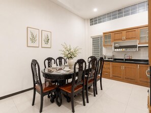 Un coin repas avec une table ronde, six chaises, un vase de fleurs et des reproductions encadrées de motifs botaniques accrochées au mur.