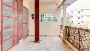 A balcony with a tiled floor, a red door, and a metal railing. - Hotel O Buckingham Canal Vijayawada (Vijayawada)