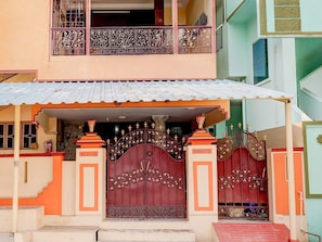 A two-story building with a gated entrance, a balcony with decorative railings, and a small porch area.