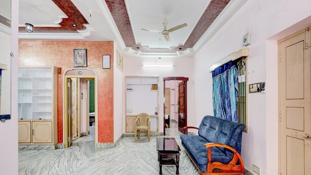 A living room with a sofa, a small table, a ceiling fan, and a door leading to another room. - Hotel O Buckingham Canal Vijayawada (Vijayawada)