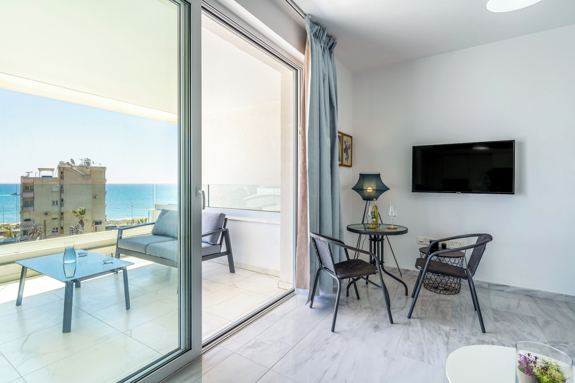 Un balcon avec un canapé et des fauteuils, une télévision et une petite table avec une lampe.