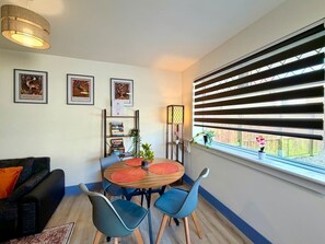 A dining area with a round table, blue chairs, a bookshelf, and a window with blinds. - 7 Spacious 1Bed House Sleeps 3 Secure Parking WiFi (Cleethorpes)