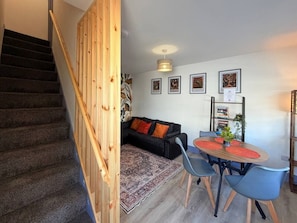 A staircase with wooden railings, a black sofa with orange cushions, a dining table with blue chairs, and framed pictures on the wall. - 7 Spacious 1Bed House Sleeps 3 Secure Parking WiFi (Cleethorpes)