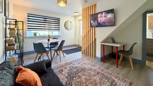 Ett modernt vardagsrum med en matplats, en tv som är monterad på väggen och en trappa som leder till ett annat våningsplan.
