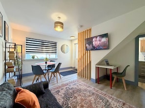 Uma sala de estar moderna com área de jantar, TV fixada na parede e escada para outro andar.