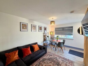 A living room with a sofa, a dining table with chairs, a bookshelf, and a window with blinds. - 7 Spacious 1Bed House Sleeps 3 Secure Parking WiFi (Cleethorpes)