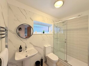Et badeværelse med marmorvæg, et rundt spejl, en vask, et toilet og et brusekabine i glas.