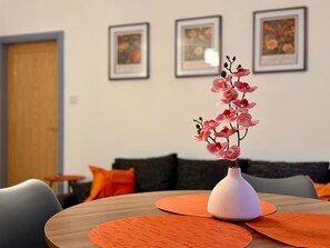 A dining area with a table, orange placemats, and a vase with pink flowers. - 4 Spacious 1-Bed Flat Sleeps 3 Secure Parking WiFi (Cleethorpes)
