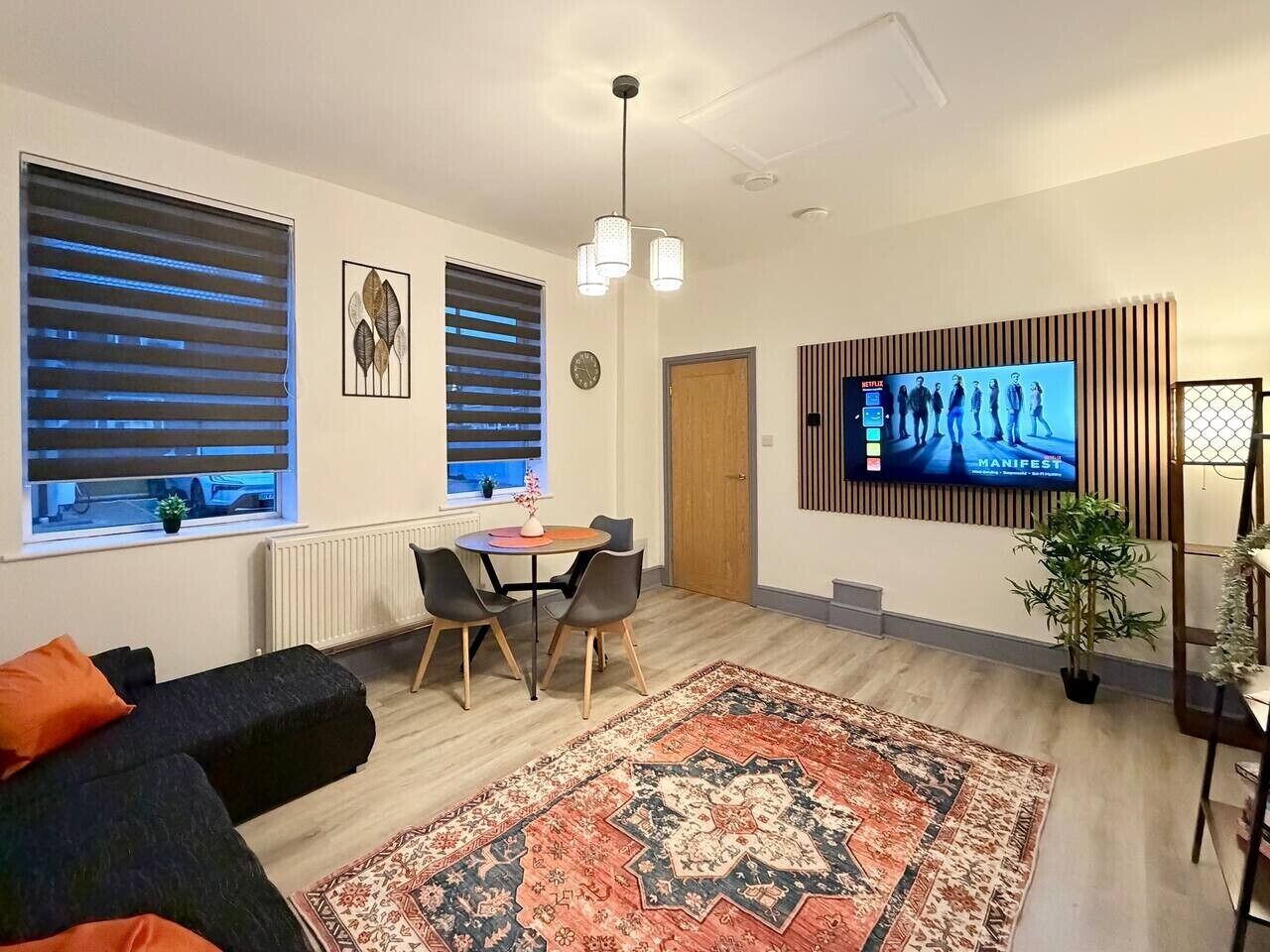 Ein modernes Wohnzimmer mit einer Couch, einem Esstisch, Stühlen, einem Fernseher und einem Teppich mit Muster.