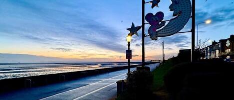 Una carretera costera con una acera peatonal, una farola y un letrero de metal decorativo con estrellas y una luna creciente.