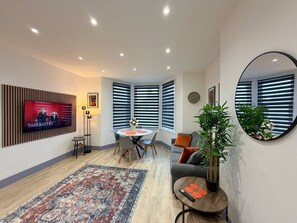 Un salon moderne avec un téléviseur, un coin repas et un grand miroir.