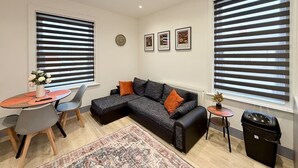 A modern living room with a sectional sofa, a dining table with chairs, and large windows with blinds. - 6 Spacious 1-Bed Flat Sleeps 3 Secure Parking WiFi (Cleethorpes)