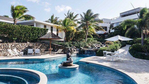 A pool with a statue, lounge chairs, and a stone wall. - Jan Sofat LUX 2BR Penthouse Pool + Mountain View (Willemstad)