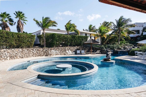 Une piscine avec un jacuzzi, des chaises longues et des palmiers.