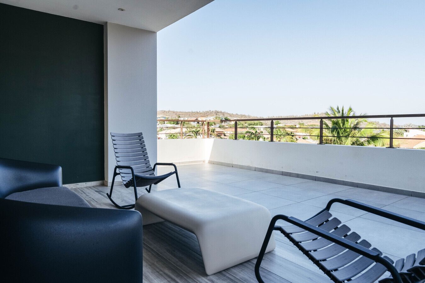 A balcony with a modern chair, a sofa, and a view of a residential area.