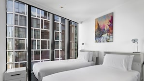 Une chambre d’hôtel moderne avec deux lits, une grande fenêtre et un tableau au mur.