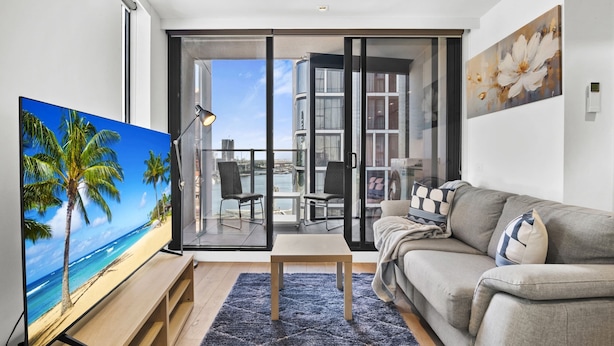 Un salon moderne doté d’un téléviseur  à écran plat, d’un canapé, d’une table basse et d’un balcon offrant une vue sur la mer.