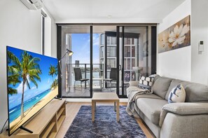 A modern living room with a flat-screen TV, a sofa, a coffee table, and a balcony with a view of the sea. - Harbour View Apartment With Pool & Gym (Melbourne)