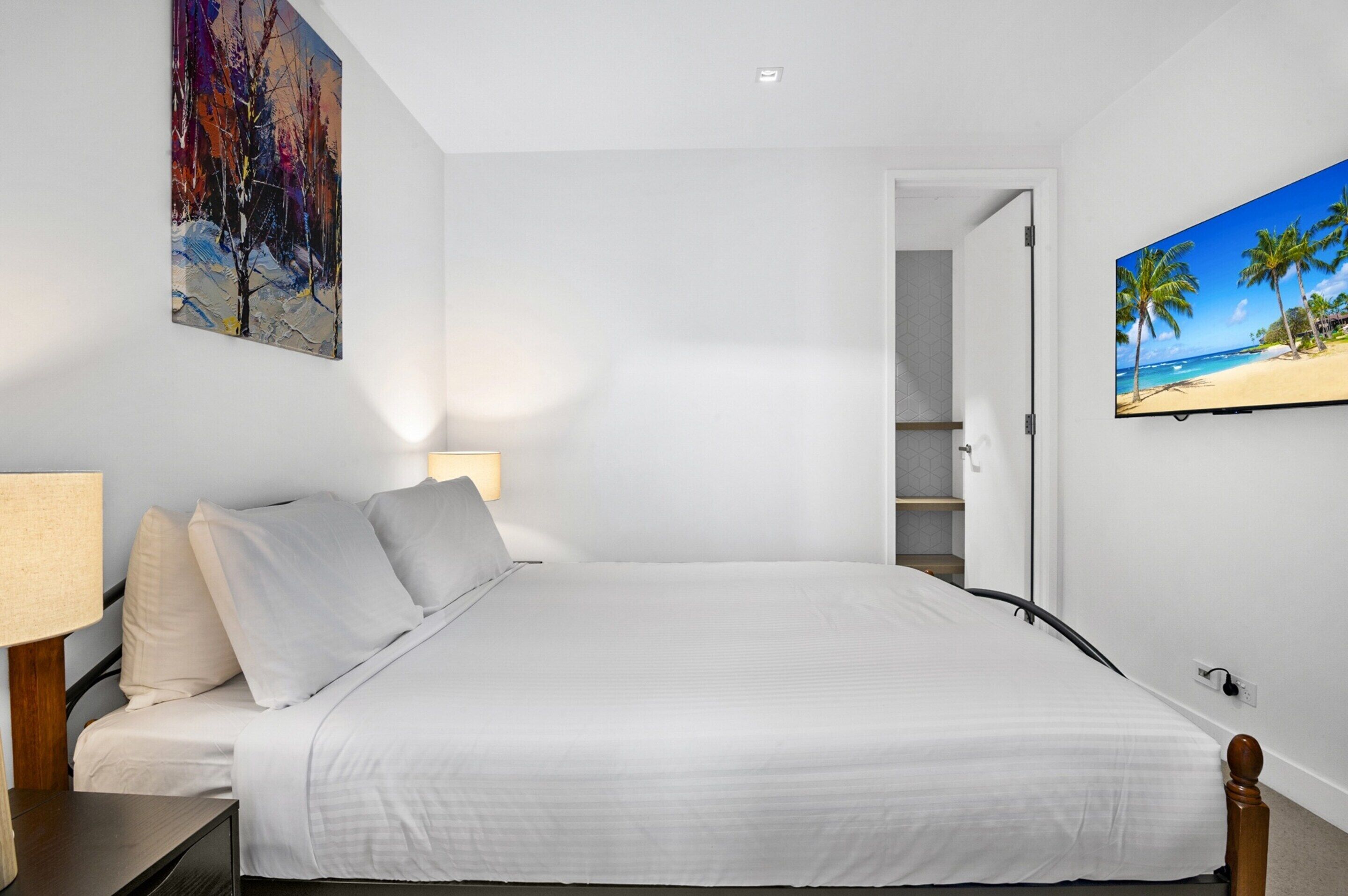 A bedroom with a bed, a nightstand, a lamp, a painting, and a TV.