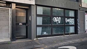 Un edifici amb una porta de garatge gran, una persiana tancada i una finestra amb grafitis.