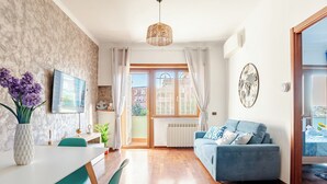 A modern living room with a sofa, dining table, chairs, a TV, and a window with curtains. - Domus Quinqueremi (roma)