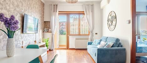 Ett modernt vardagsrum med en soffa, ett matbord, stolar, en tv och ett fönster med gardiner.