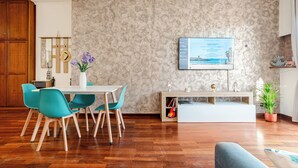 A modern living room with a dining area, a flat-screen TV mounted on the wall, and a potted plant. - Domus Quinqueremi (roma)