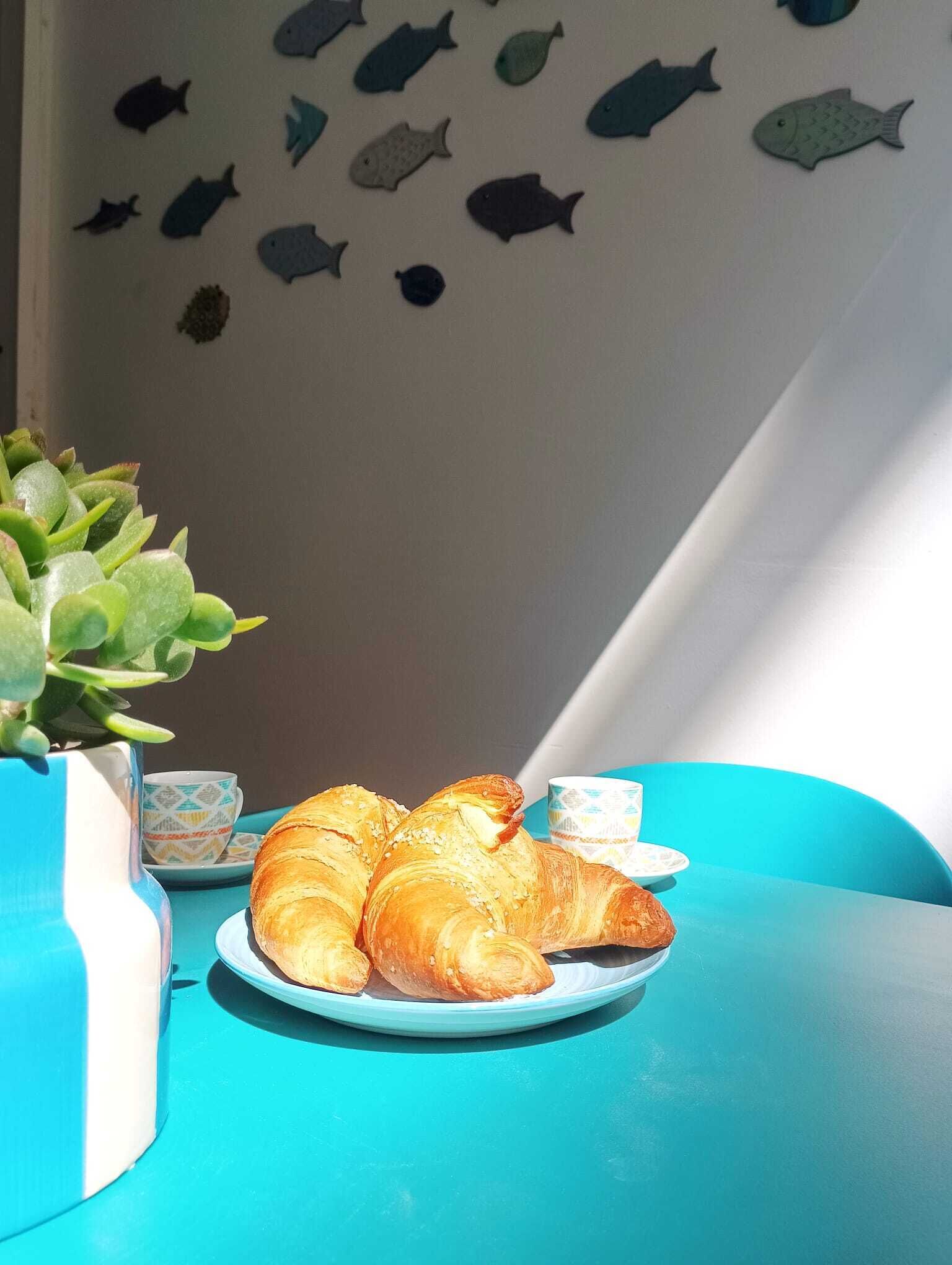 Une table avec une assiette de croissants, une petite tasse et un mur décoratif orné de motifs de poissons découpés.
